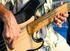 A person in a floral shirt plays an electric bass guitar outdoors.