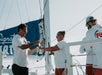 People enjoying a drink on a sailboat, with a blue sail banner in the background.
