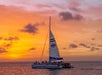 A catamaran named Fury sails on the ocean at sunset with passengers aboard, under a sky with orange and purple hues.