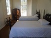 A room with several windows, two wooden vintage beds, and an armoire for guests at Felicity Plantation in Vacherie, LA