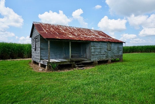 An old worn building with wooden slat walls, and a rusted tin roof on a sunny day at the Felicity Plantation in Vacherie, LA