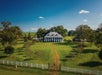 Aerial view looking down on the St. Joseph Plantation with trees around it and a lush green lawn and a blue sky overhead in Vacherie.