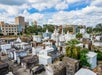 Aerial view of an above-ground cemetery with white tombs, surrounded by trees and buildings under a cloudy sky.