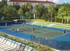 Four people playing tennis on a blue court surrounded by greenery and buildings.