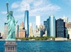 Statue of Liberty in the foreground with the New York City skyline and skyscrapers in the background, viewed across the water.