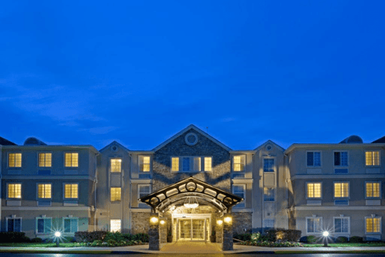Illuminated hotel building at dusk with a stone archway entrance and lit windows against a deep blue sky.