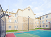 Outdoor basketball court beside a three-story beige apartment building with stone accents and windows.