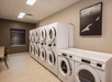 A laundry room with multiple white washing machines and dryers lined up against the wall. A framed black and white photo hangs above the machines.