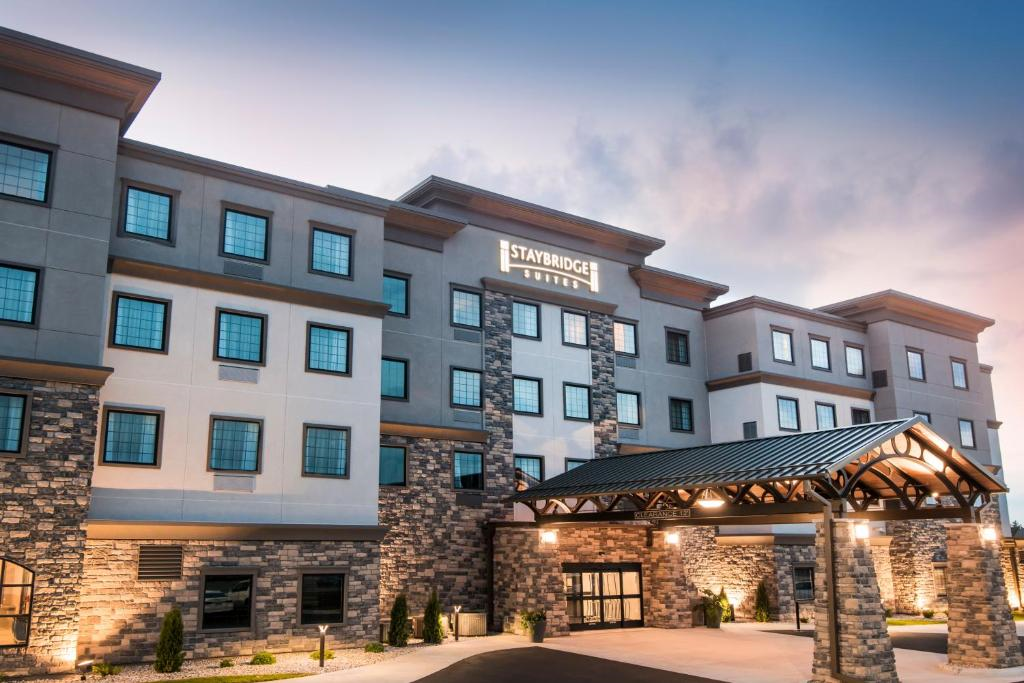 Front view of a modern hotel with a mix of stone and stucco facade, featuring a covered entrance and lit sign against a dusk sky.