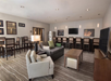Modern lounge area with a sofa, armchair, coffee table, TV, and bar seating. Walls are adorned with framed artwork. Neutral colors and patterned carpet enhance the serene ambiance.