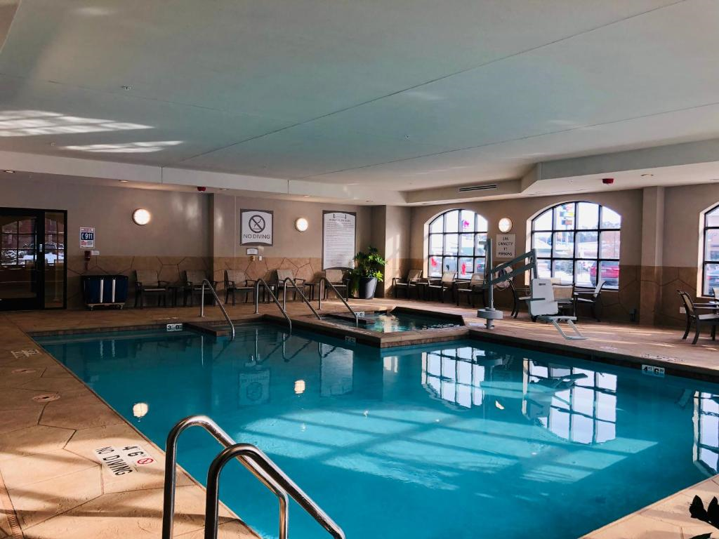 Indoor swimming pool with clear water, surrounded by poolside chairs, safety signage, and windows allowing natural light.