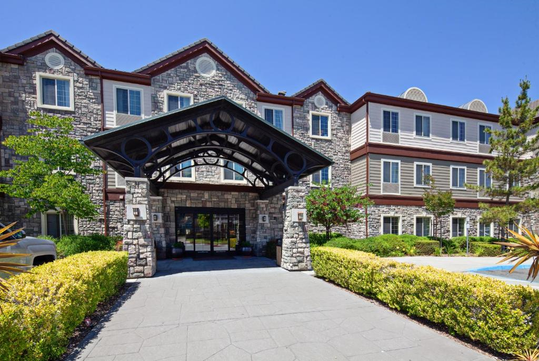 Stone and brick hotel exterior with arched entrance, surrounded by greenery and a clear blue sky.