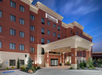 Exterior of a Staybridge Suites hotel at dusk, featuring a multi-story brick building with a prominent entrance and well-lit surroundings.