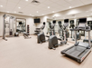 A gym with treadmills, elliptical machines, a multi-function exercise station, balance balls, and free weights. Large mirror and television on the walls.