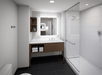 Modern bathroom with a glass-enclosed shower, wall-mounted vanity with storage space, and a large rectangular mirror above the sink. Black tiled floor and white walls.