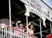 Two women wave from the upper deck of the Steamer Natchez riverboat in New Orleans, standing behind a white railing under a large sign.