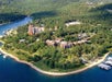 Aerial view of a forested peninsula with several buildings near a lake, surrounded by dense trees and water with a few docks.