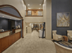 Hotel lobby with a check-in counter on the left, beige chairs and a table on the right, and a hallway leading to a dining area. A large framed artwork hangs on the wall.