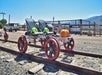 Two small carts with red wheels on railroad tracks, near a strawberry farm sign and parked vehicles in the background.