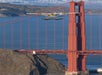 A seaplane flies near the towers of the Golden Gate Bridge in San Francisco, with water and hills visible in the background.