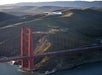 A white airship flies above green hills near the Golden Gate Bridge in San Francisco, with the bridge and coastline visible below.