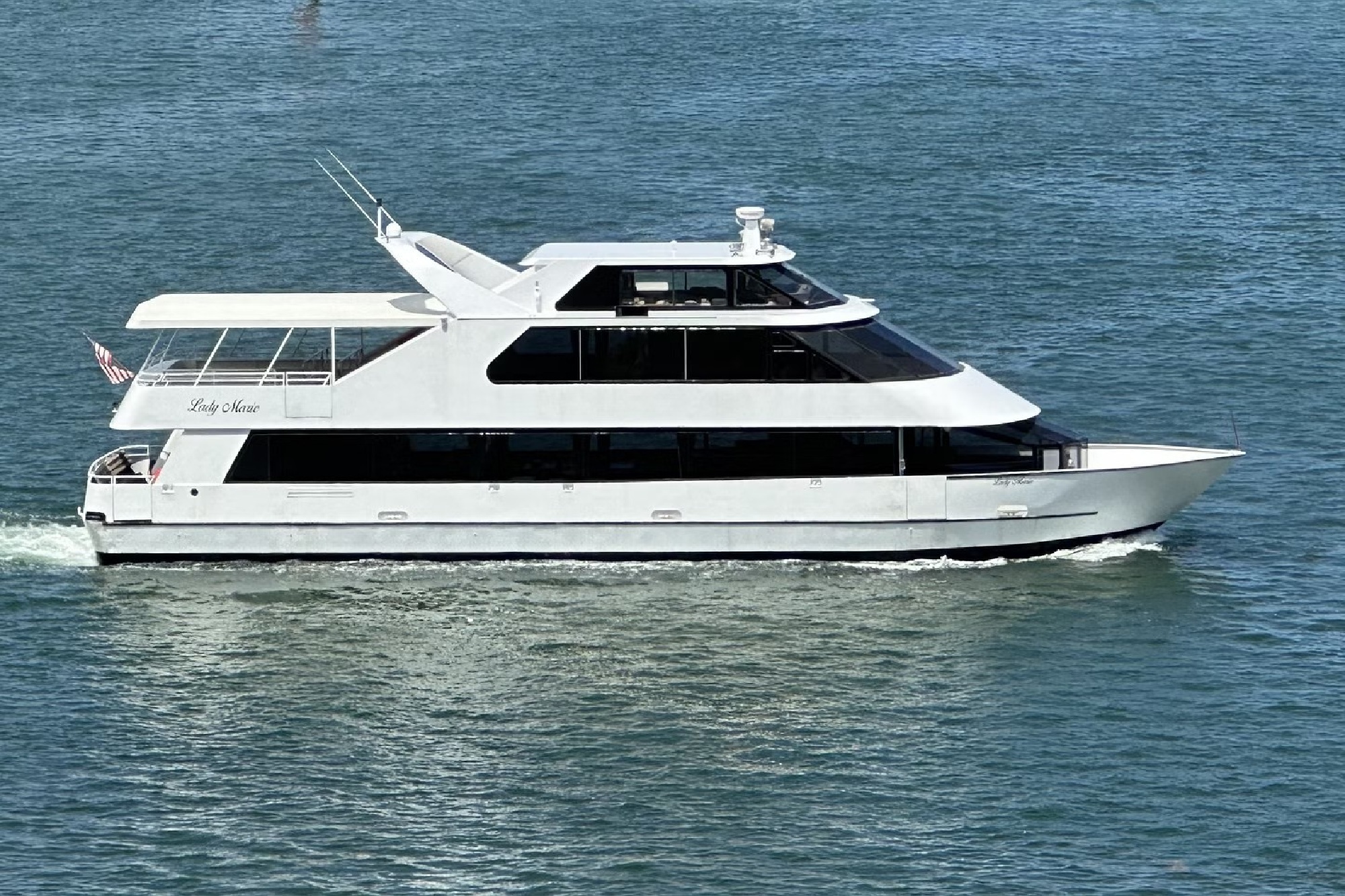 A white yacht cruises on clear blue water, displaying an American flag at the rear.