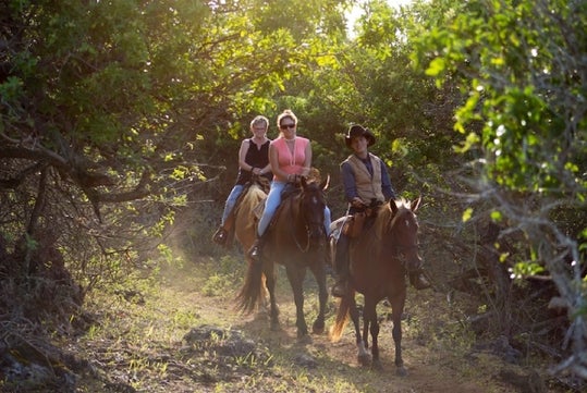 Two riders and a guide on horseback riding  along a mountain trail