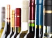 A close-up of various wine bottles in a row, showing their different colored necks and caps against a white background.