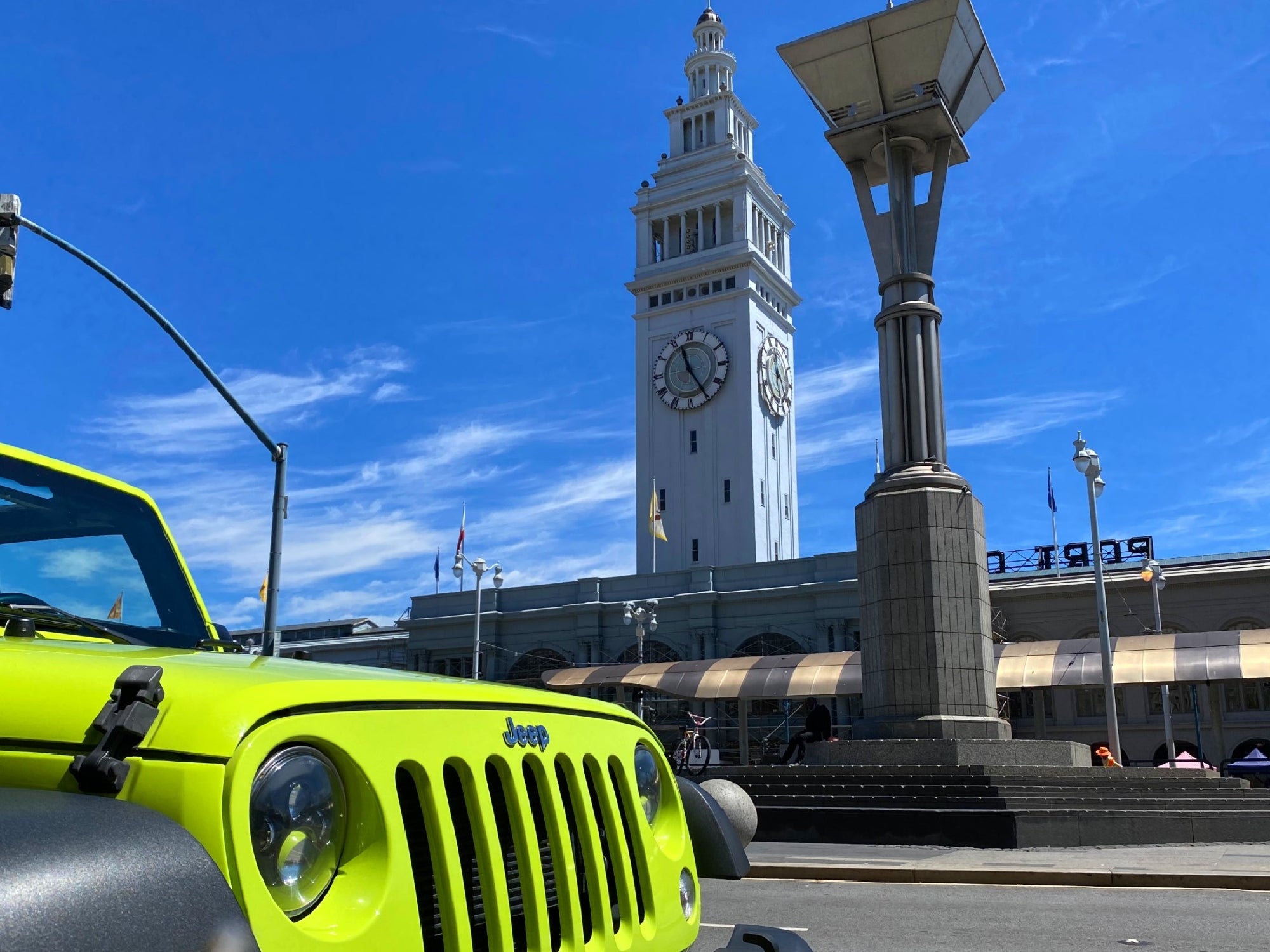 A bright green Jeep parked near the Ferry Building with its clock tower under a blue sky in San Francisco.