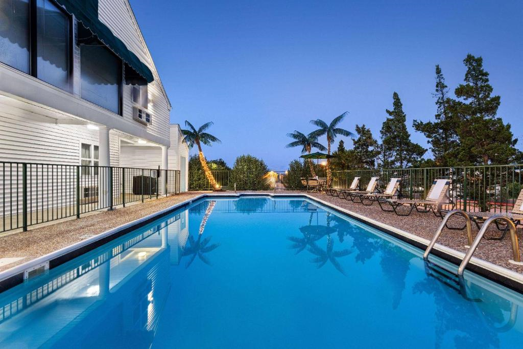 Outdoor pool with clear blue water, surrounded by lounge chairs and palm trees, adjacent to a white building under a clear evening sky.