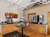 A breakfast buffet area with coffee machines, cereal dispensers, a juice machine, and a table with fruit cups on a wooden floor. Wall art decorates the beige walls.