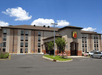 View of the front exterior of the Super 8 by Wyndham Mount Laurel with trees and pink bushes out front and a blue cloudy sky overhead.