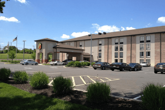 View of the front exterior of the Super 8 by Wyndham Mount Laurel with several cars in the parking lot and a blue cloudy sky overhead.