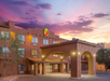 Exterior view of a Super 8 hotel at sunset, featuring a southwestern-style facade, arched entrance, and illuminated signage.