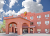 Exterior of a Super 8 hotel with an archway entrance, red stucco facade, and a cloudy blue sky.