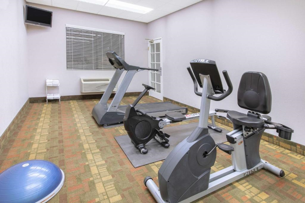 Small gym room with a treadmill, stationary bike, and a blue exercise ball. A TV is mounted on the wall. The room has gray walls and a window with blinds.