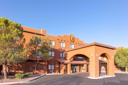 Exterior of a Super 8 hotel with a southwestern-style architecture, featuring an archway entrance, tan stucco walls, and surrounding trees against a clear blue sky.