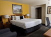 Hotel room with a large bed, white linens, two lamps, an armchair, and framed pictures on the walls.