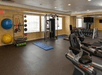 A gym with exercise equipment, including stationary bikes, a weight machine, free weights, exercise balls, and yoga mats on the floor.