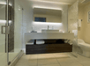 Modern bathroom featuring a large mirror, floating sink with storage, glass shower, and toilet. The wall has a wavy texture and soft lighting.