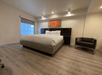 Modern bedroom with a large bed, white bedding, wooden floors, and an armchair. A colorful abstract painting hangs above the bed, and recessed lighting brightens the space.