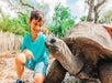 A young boy in a bright blue shirt smiling and petting a Giant Tortoise at ZooTampa at Lowry Park.