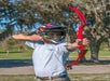 A man displays a red bow and arrow while wearing a helmet and safety glasses