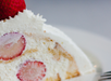 A close-up of a slice of strawberry shortcake with layers of whipped cream, whole strawberries inside, and a whole strawberry on top.