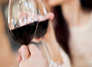 Two people clinking glasses of red wine, with one person in focus holding a glass in the foreground and the other slightly blurred in the background.