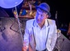 A man with a hat and white jacket performs a magic trick