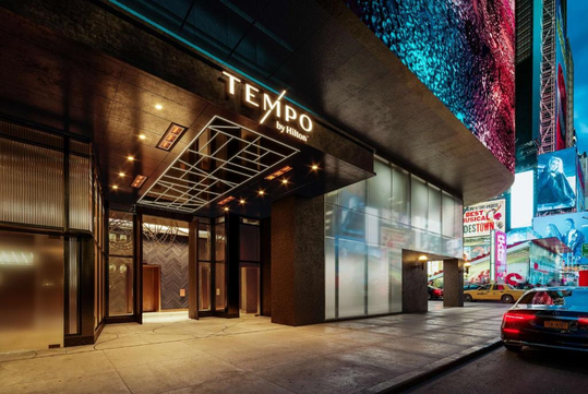 Entrance of Tempo by Hilton hotel at night with illuminated signs and a parked car on the street.