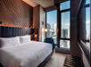 A modern hotel room with a large bed, stylish wall design, and floor-to-ceiling windows offering a cityscape view.