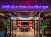 A cozy room with a wooden table, chairs, and plants. Neon sign above reads, "Live life with no excuses, travel with no regret.