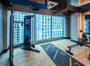 A modern gym with a cable machine and rowing machine, wood flooring, and a large window overlooking a building.